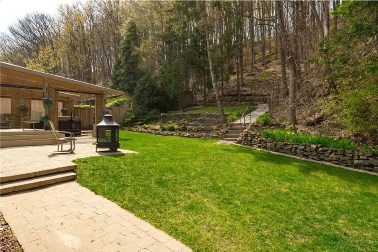 Backyard lawn with a stone retaining wall and steps up toward the escarpment