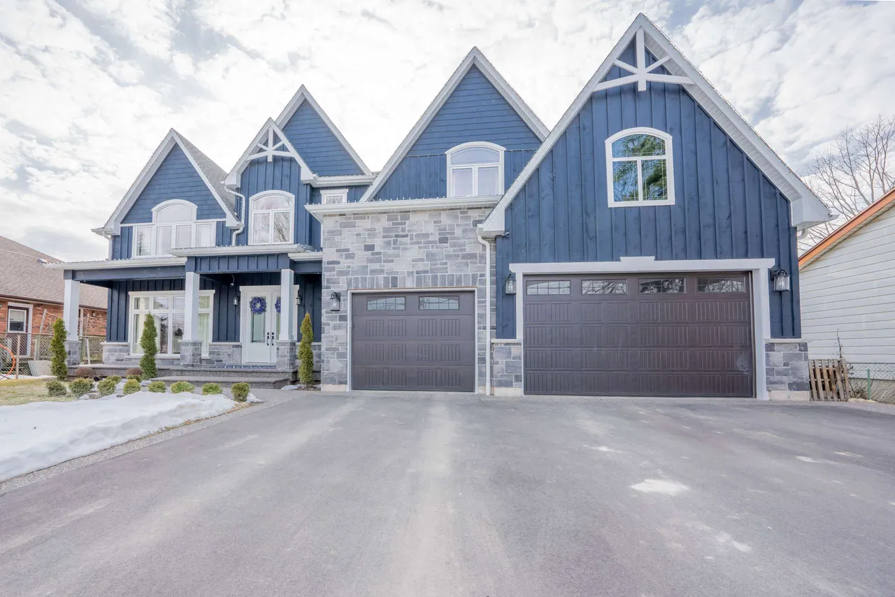 Front exterior of a two-storey custom-built home on Springbrook Avenue with blue board-and-batten siding, stone accents, and a triple-car garage