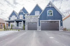 Front exterior of a two-storey custom-built home on Springbrook Avenue with blue board-and-batten siding, stone accents, and a triple-car garage