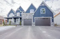 Front exterior of a two-storey custom-built home on Springbrook Avenue with blue board-and-batten siding, stone accents, and a triple-car garage
