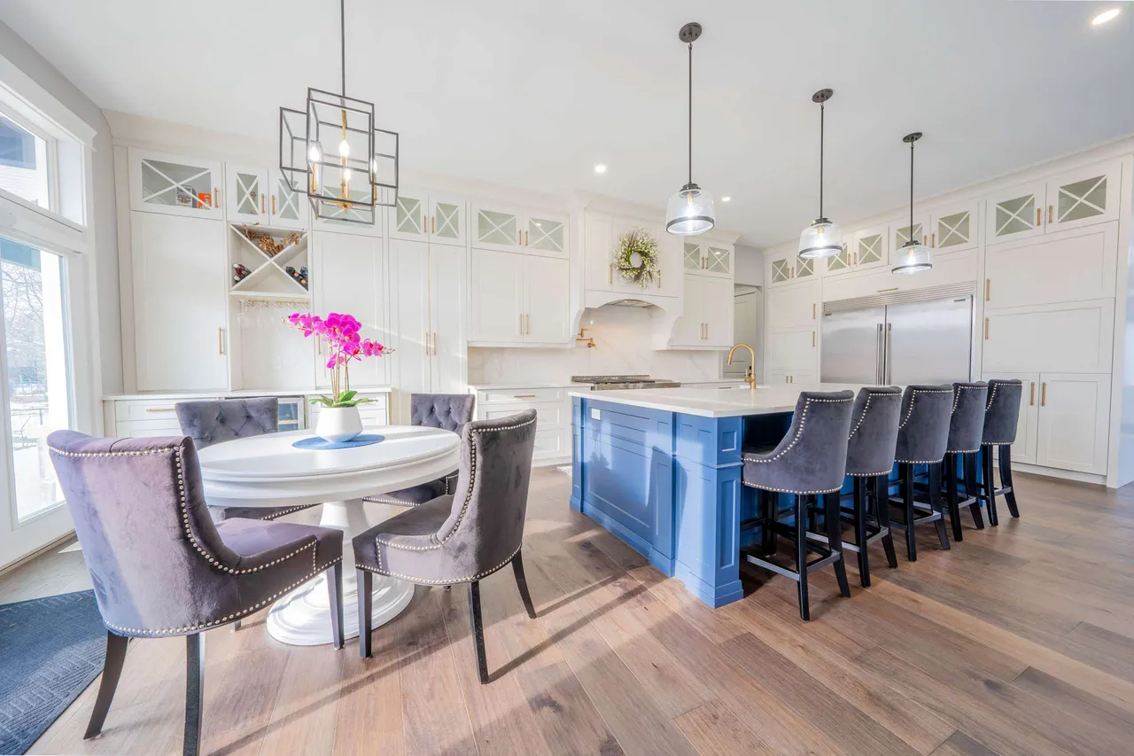 Open-concept kitchen with a blue centre island, white cabinetry, and a round breakfast table
