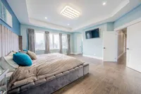 Primary bedroom with a tray ceiling, wall-mounted TV, and large windows