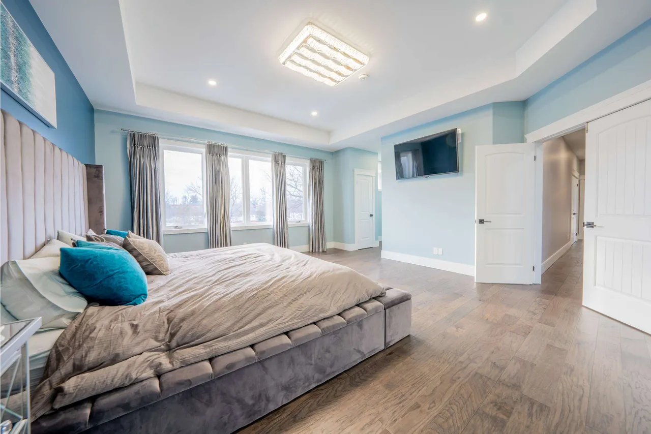 Primary bedroom with a tray ceiling, wall-mounted TV, and large windows