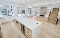 Open-concept kitchen with a waterfall island, custom cabinetry, gas fireplace, and an open staircase