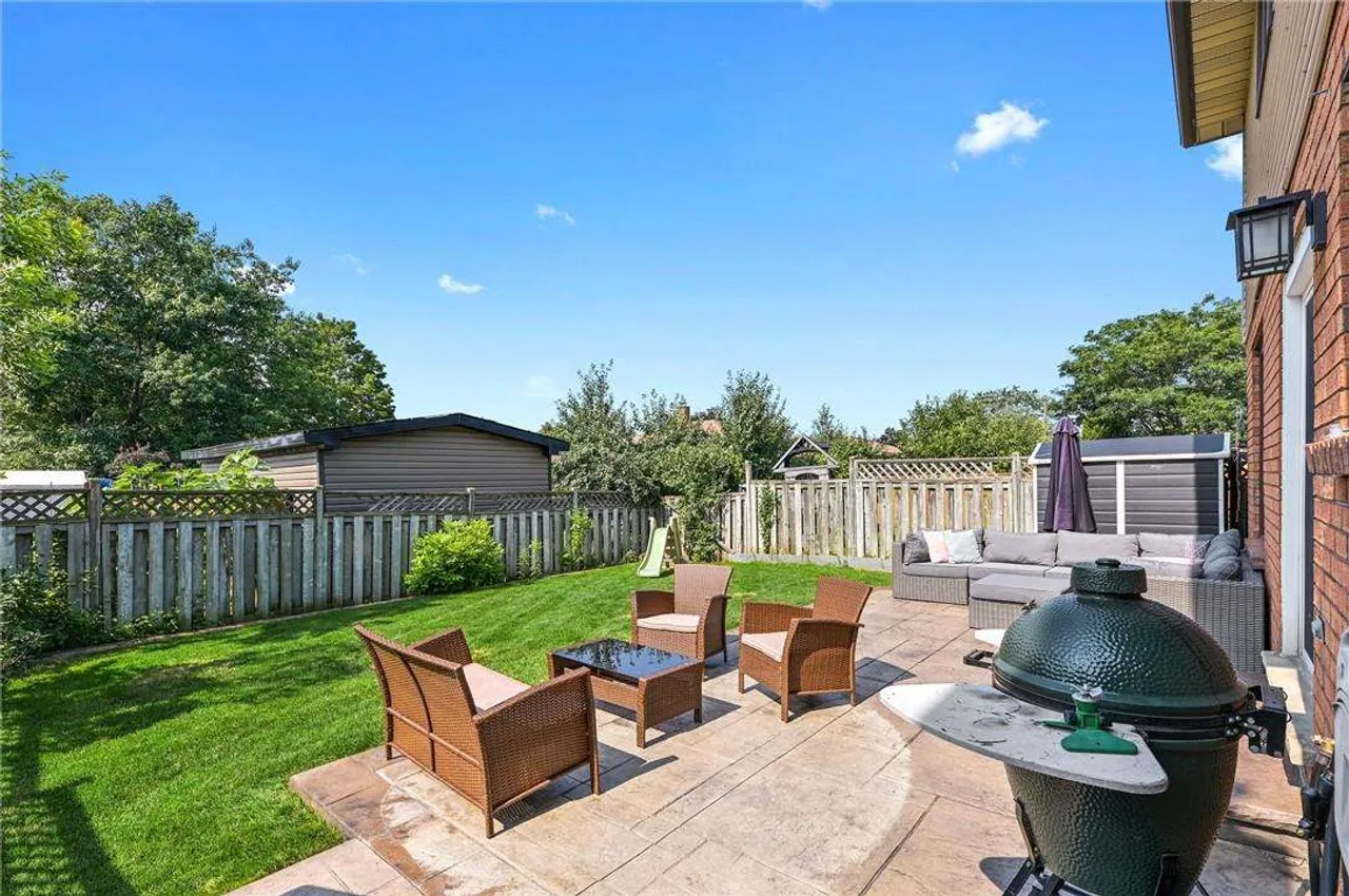 Backyard patio seating area with mature trees and a storage shed